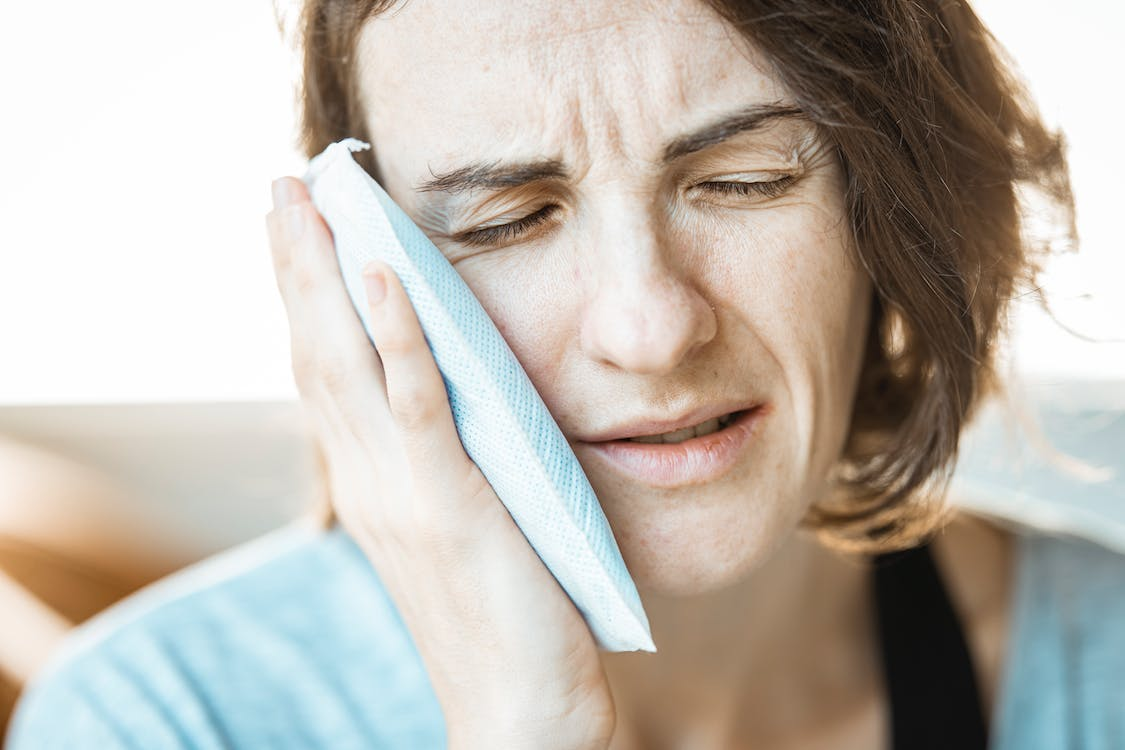 A woman is putting a cold compress on her cheeks to alleviate toothache